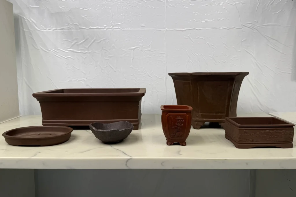 Selection of unglazed bonsai pots of different shapes and sizes on marble indoors
