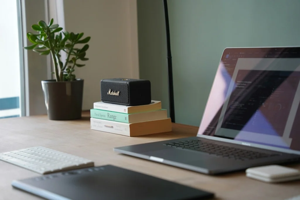 Office desk with laptop, books and amplifier neatly arranged, with a small jade plant bonsai in the corner